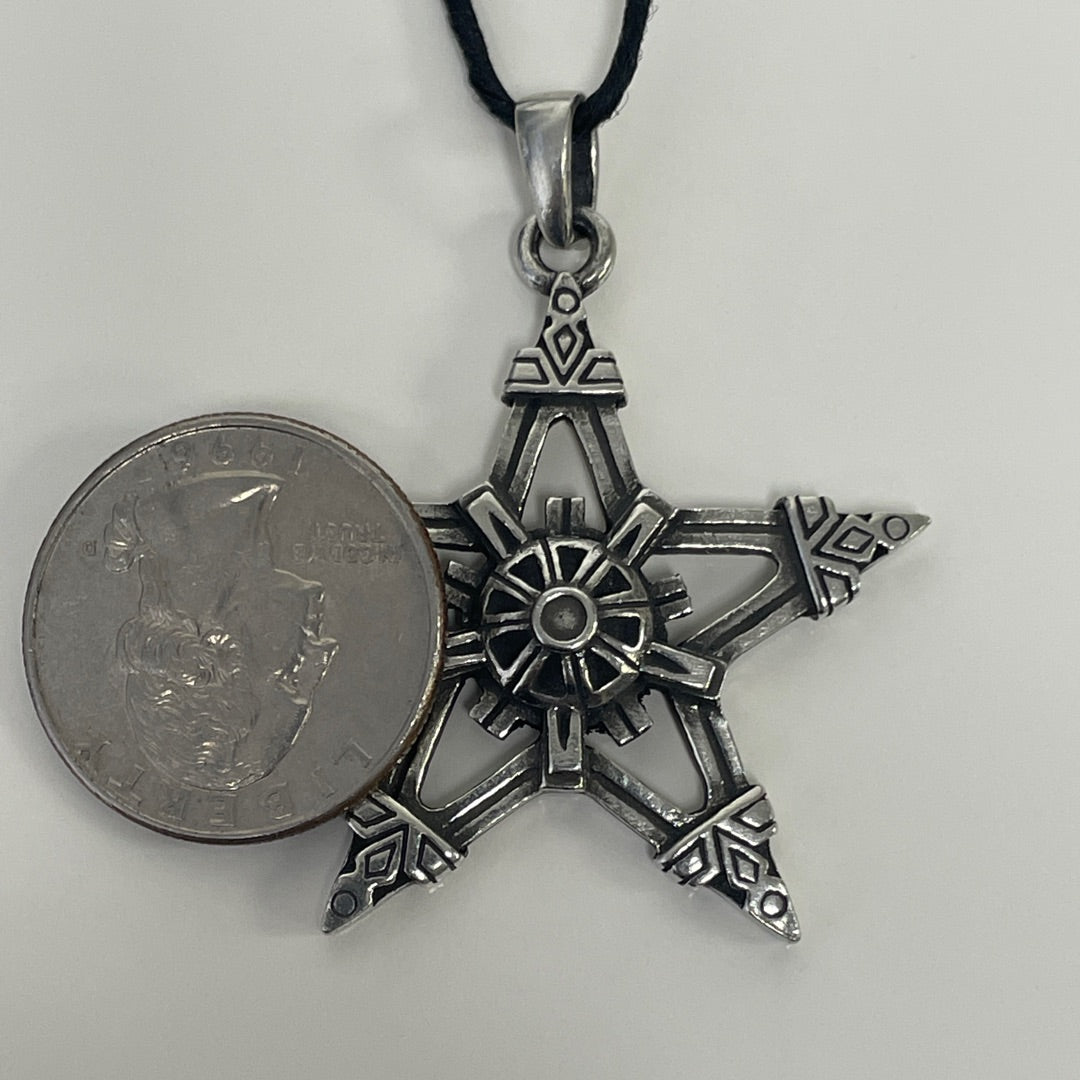 An antique silver-toned star-shaped pendant necklace with a black cord, shown next to a US quarter coin for scale on a light gray background.
