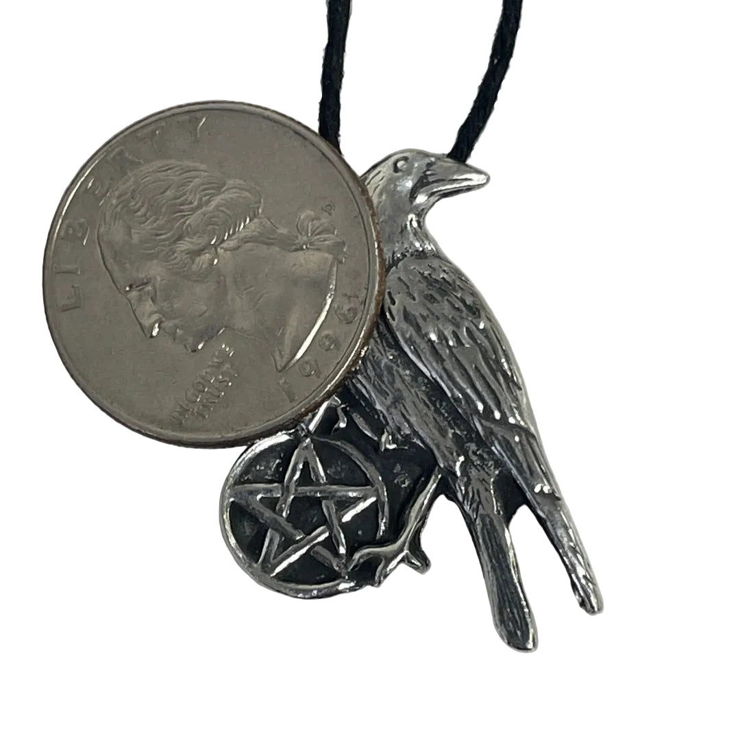 A silver-toned raven pendant necklace with a pentagram charm, shown next to a US quarter for scale on a plain light background.