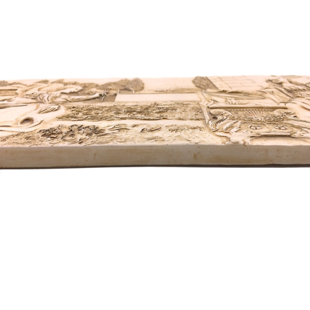 A rectangular beige stone or concrete relief plaque featuring embossed classical scenes and figures, shown against a plain white background.