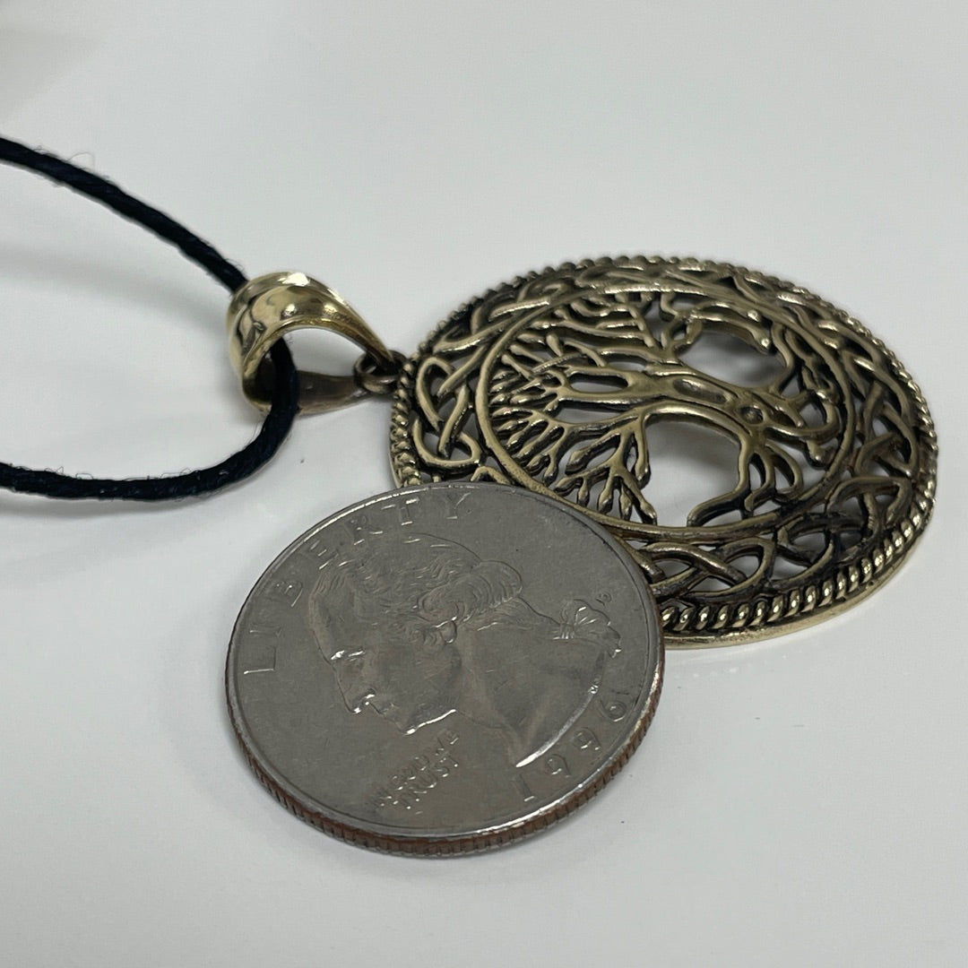 A round bronze Celtic knot tree of life pendant necklace on a black cord, shown next to a US quarter coin for scale on a white background.