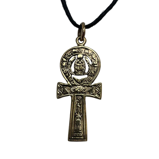 An ancient Egyptian Ankh pendant in an antique gold finish, hanging from a black cord on a neutral gray background.