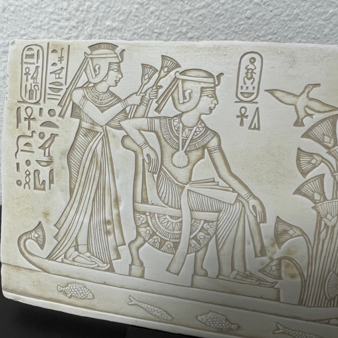 Ancient Egyptian wall relief of pharaoh and wife on a raft with hieroglyphs and papyrus