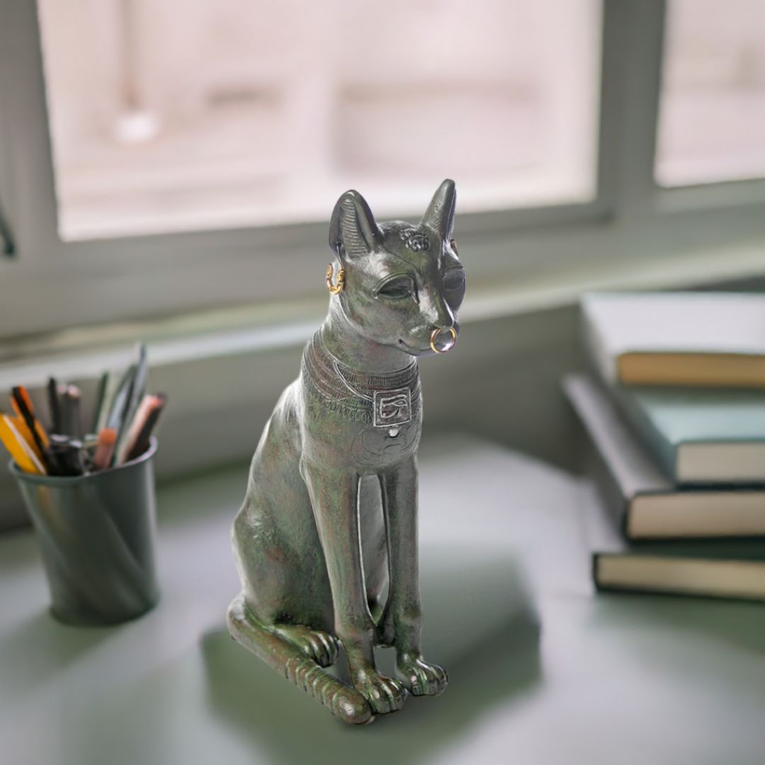 Egyptian Bastet cat statue replica with gold jewelry on desk near books and pencils