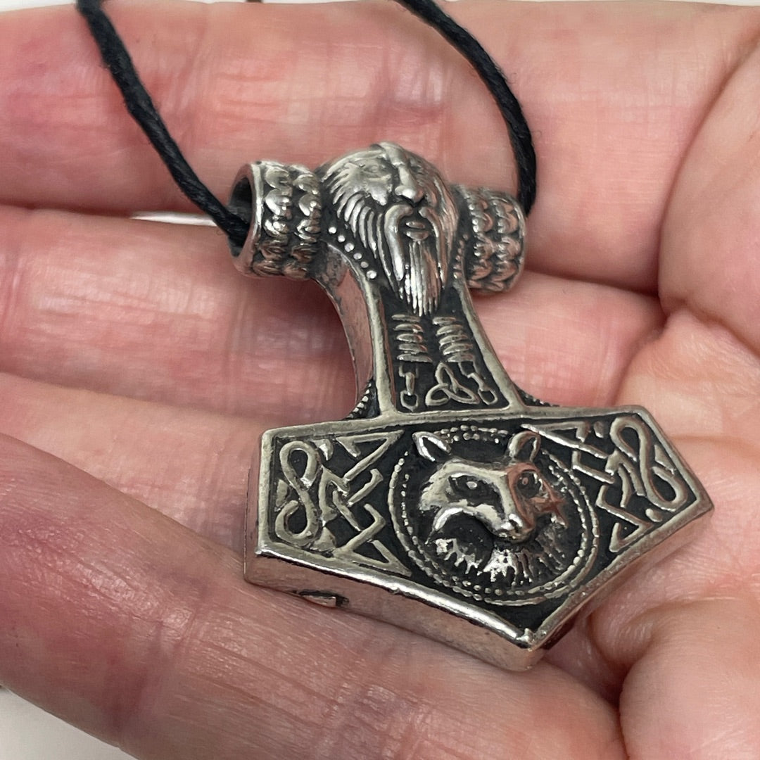 A silver-toned Viking-style mace pendant with an engraved bearded figure and wolf motif, hanging from a black cord and held in a person's hand.