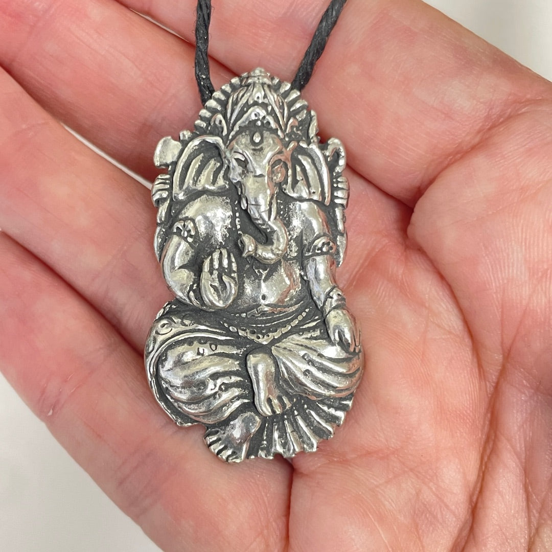 A detailed silver Ganesha pendant on a black cord, held in a person's hand.