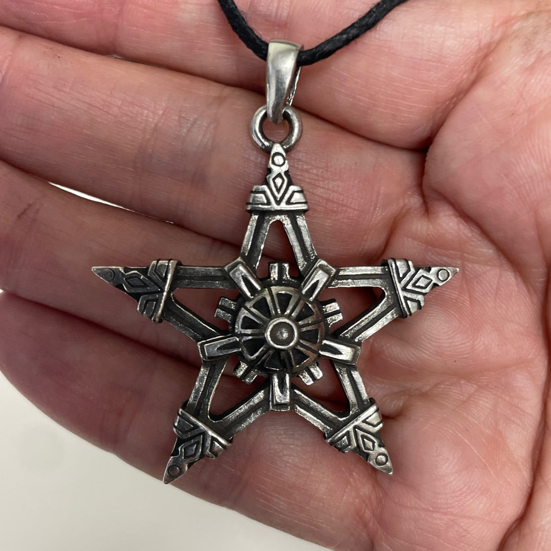 A silver-toned five-pointed star pendant with intricate geometric carvings, hanging from a black cord and held in a person's hand.