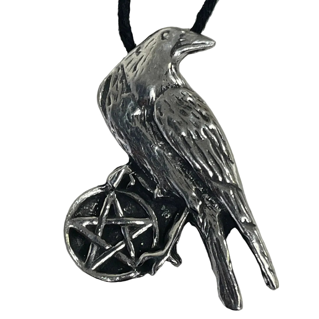A silver raven pendant with a black pentagram design on its body, hanging from a black cord against a plain light gray background.